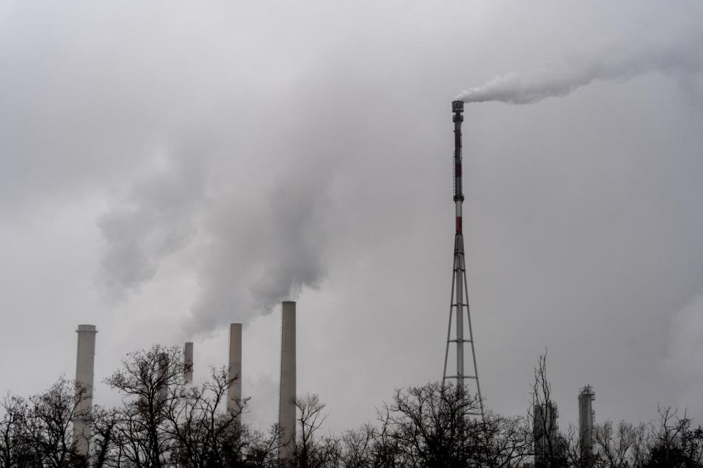 Black-and-white photo of the chimneys at a refinery emitting thick white smoke under a cloudy sky