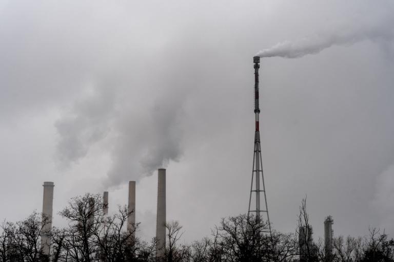 Black-and-white photo of the chimneys at a refinery emitting thick white smoke under a cloudy sky