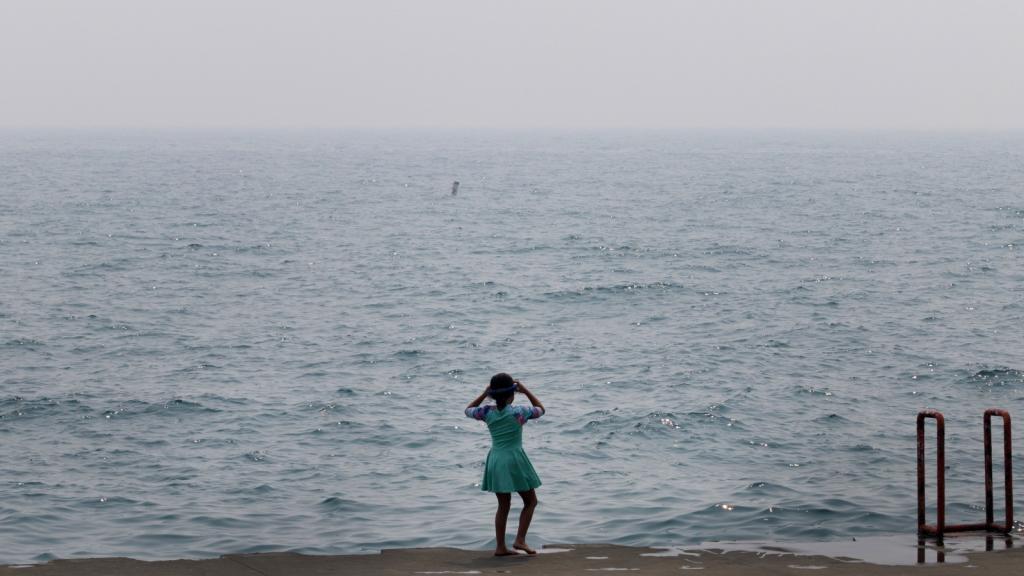 A child stands in front of a murky sea