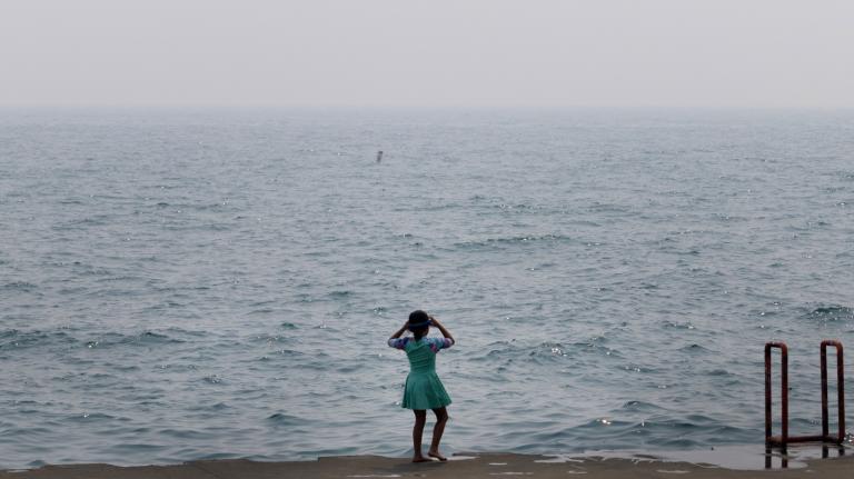 A child stands in front of a murky sea