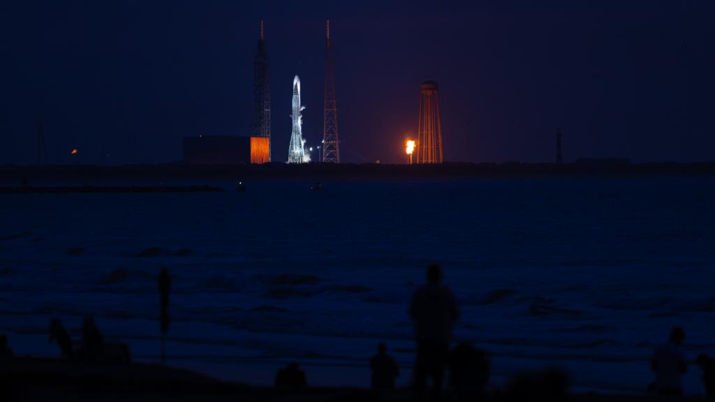 Photo of people watching a rocket launch at night