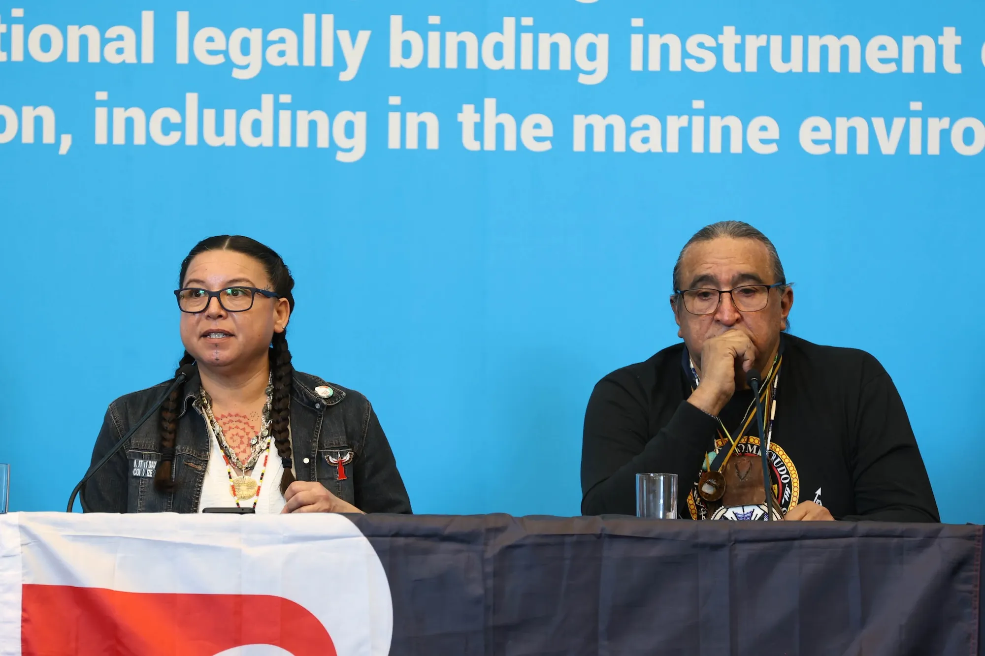 A woman and Juan Mancias sit on a panel in front of a bright blue backdrop