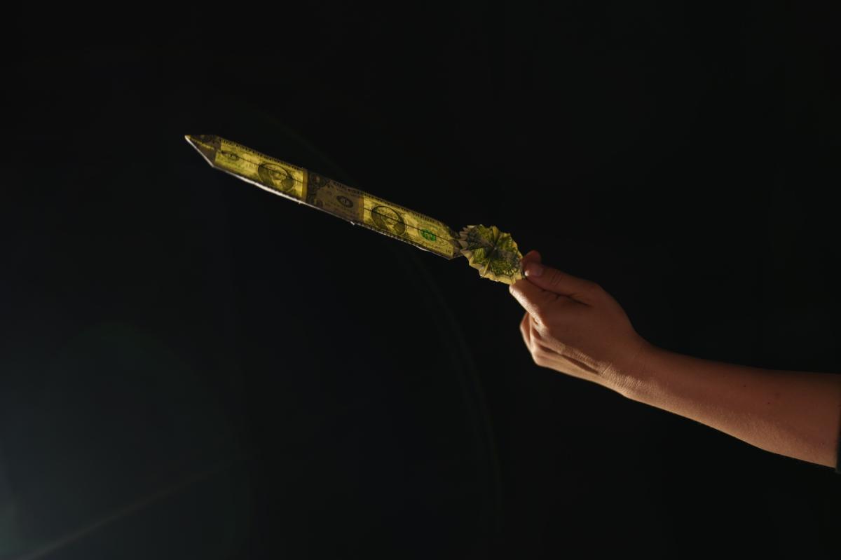 A hand holds out a feather made of two dollars folded bills
