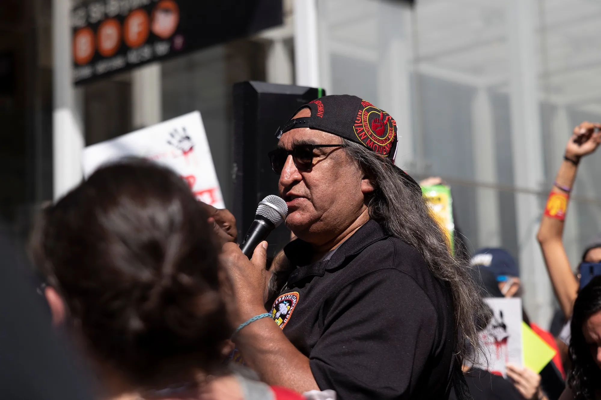Juan Mancias holds a microphone and wears a backward baseball cap at a rally in New York