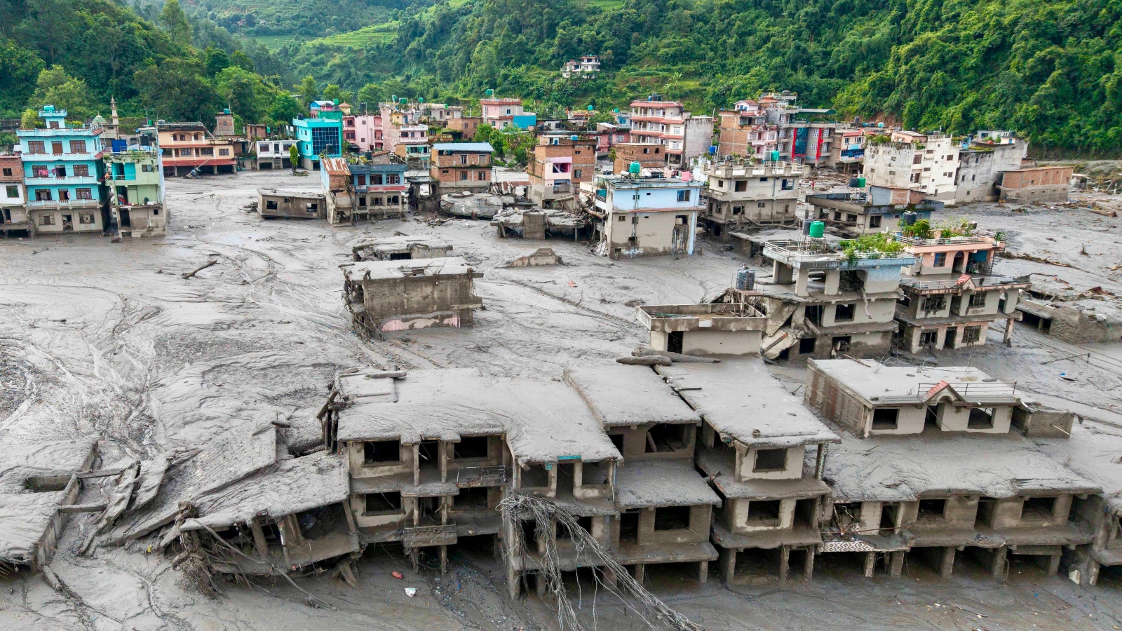 A colorful town is engulfed in mud as green mountains loom in the background
