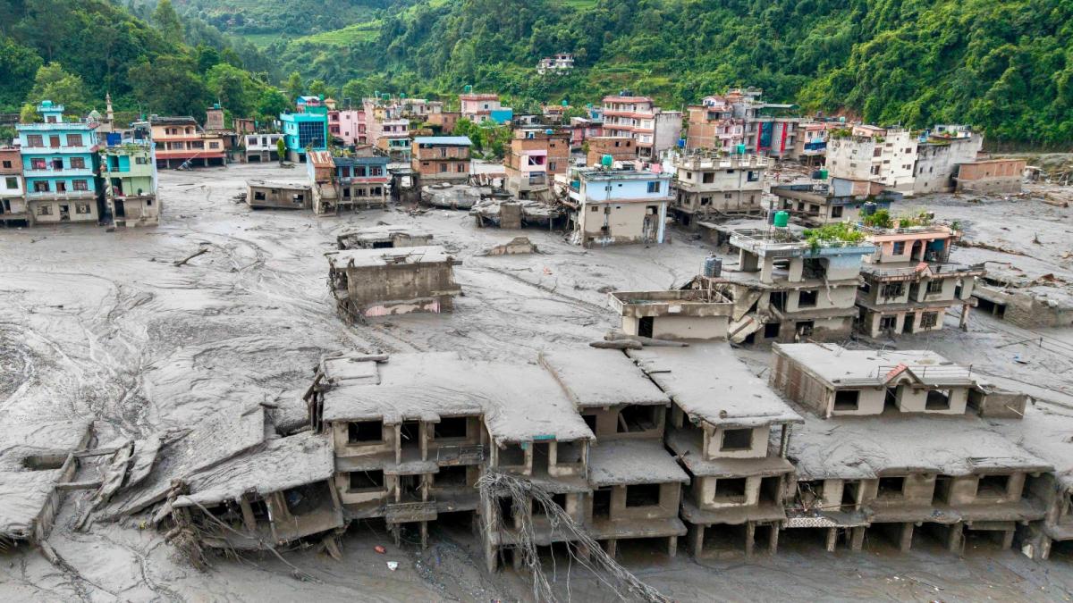 A colorful town is engulfed in mud as green mountains loom in the background