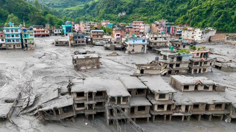 A colorful town is engulfed in mud as green mountains loom in the background