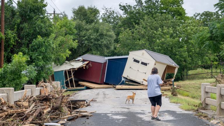 A woman and a dog stand in front of a flood-damaged house in Texas