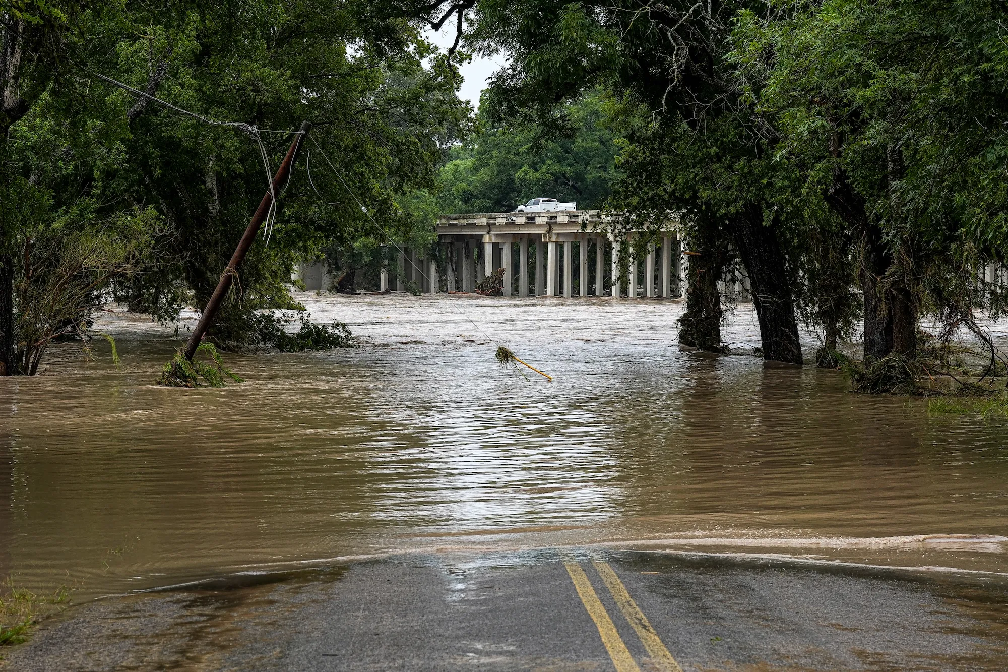 A flooded roadway near a large city building with trees out front
