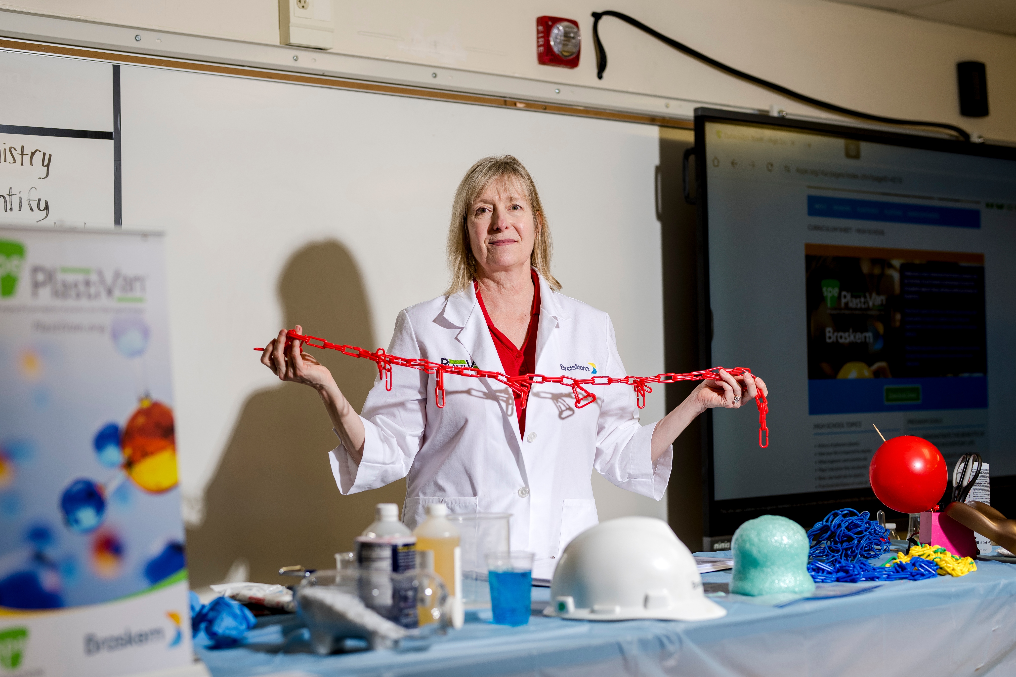 Eve Vitale, a blond middle-age woman in a lab coat holding a red chain during a science experiment inside a classroom