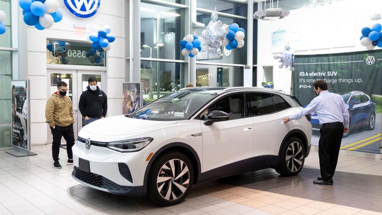 A salesperson showing a Volkswagen electric car to potential buyers at a dealership