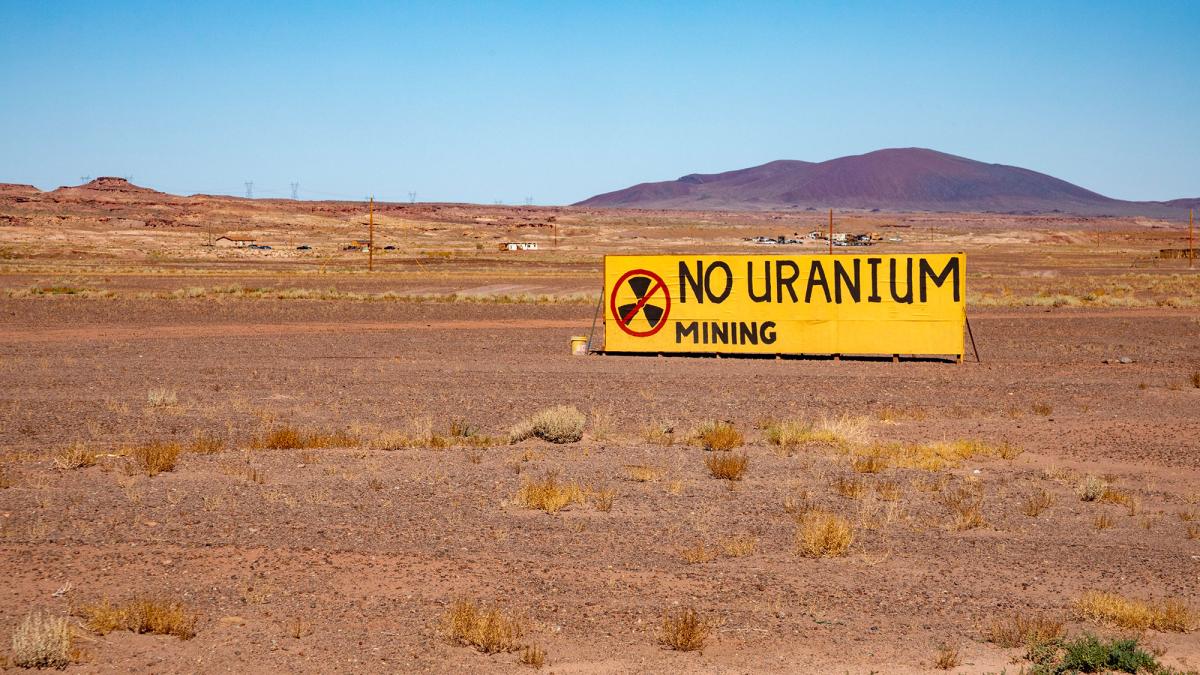 A yellow sign reading No Uranium Mining against a desert landscape with red dirt and a hill in the background
