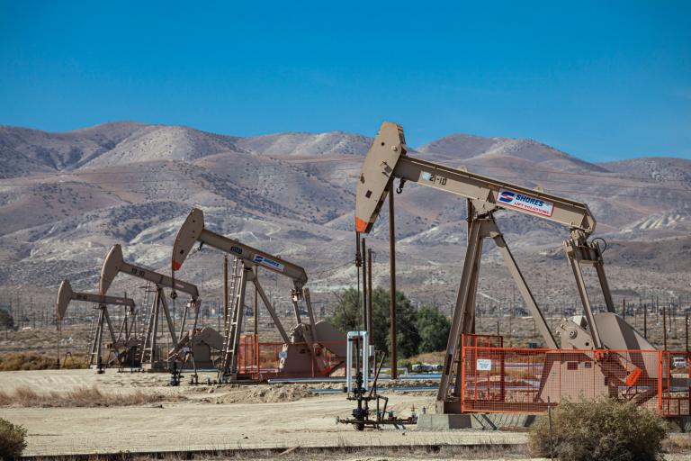 A row of oil pumpjacks in a field surrounded by mountains