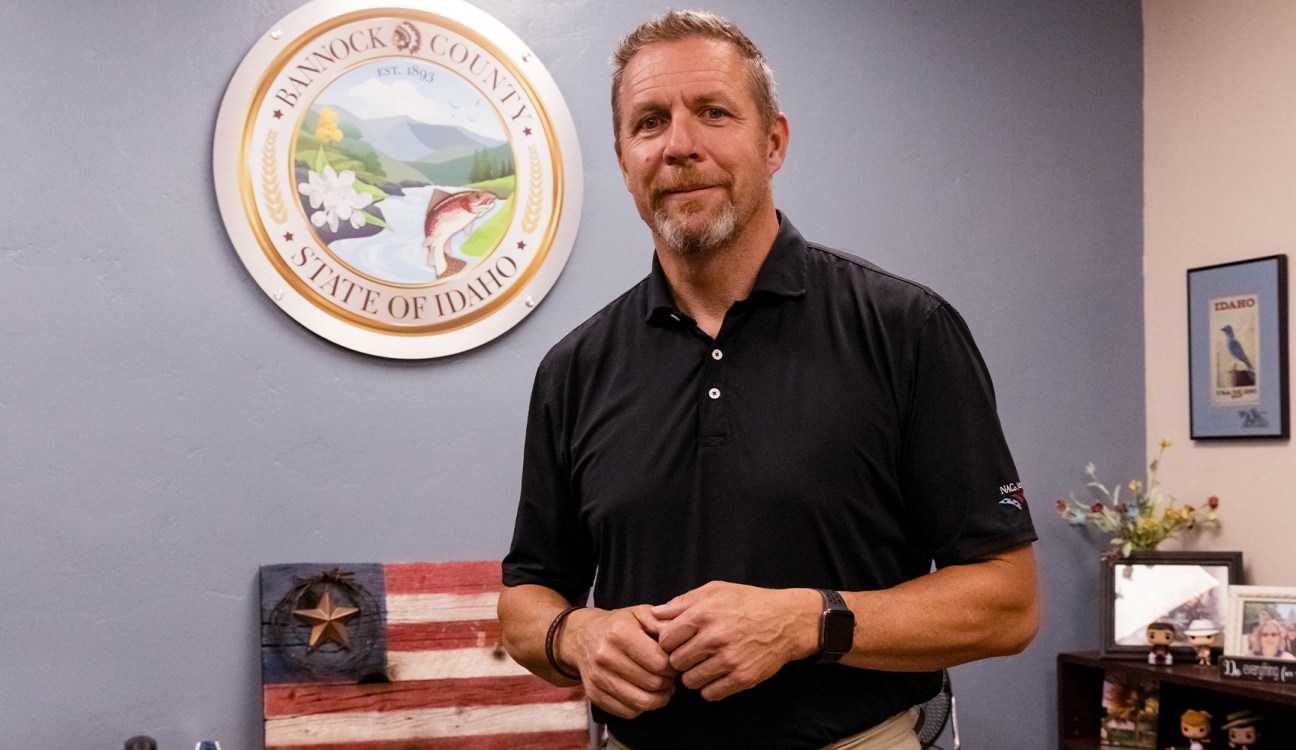 A man wears a black shirt in front of an American flag