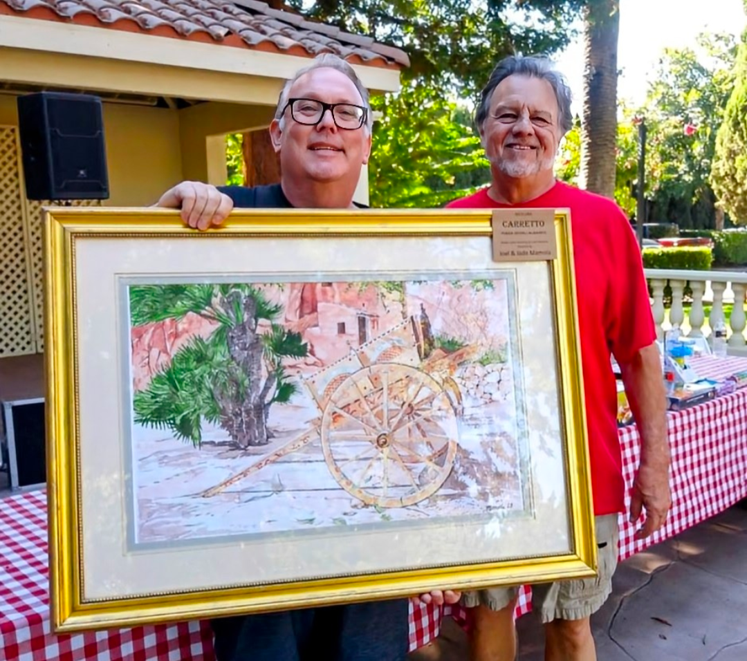 A man holds up a gold-framed painting of a town