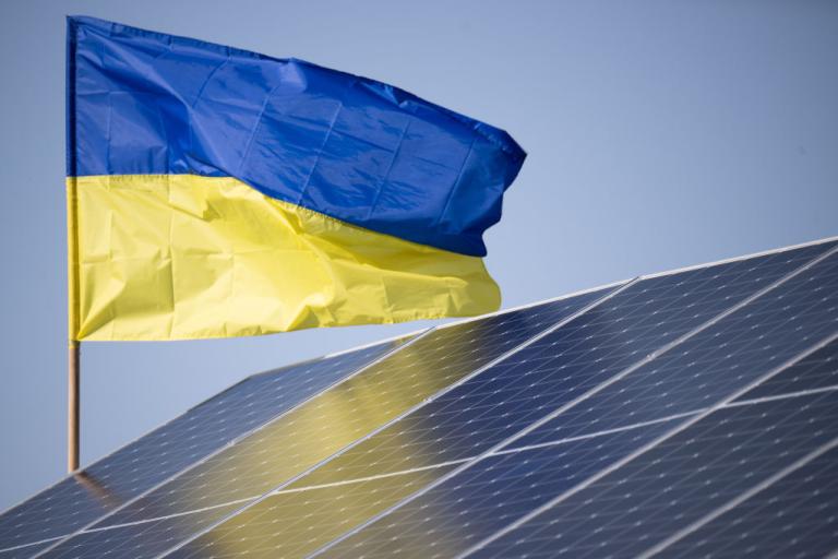 A Ukrainian flag flies behind solar panel