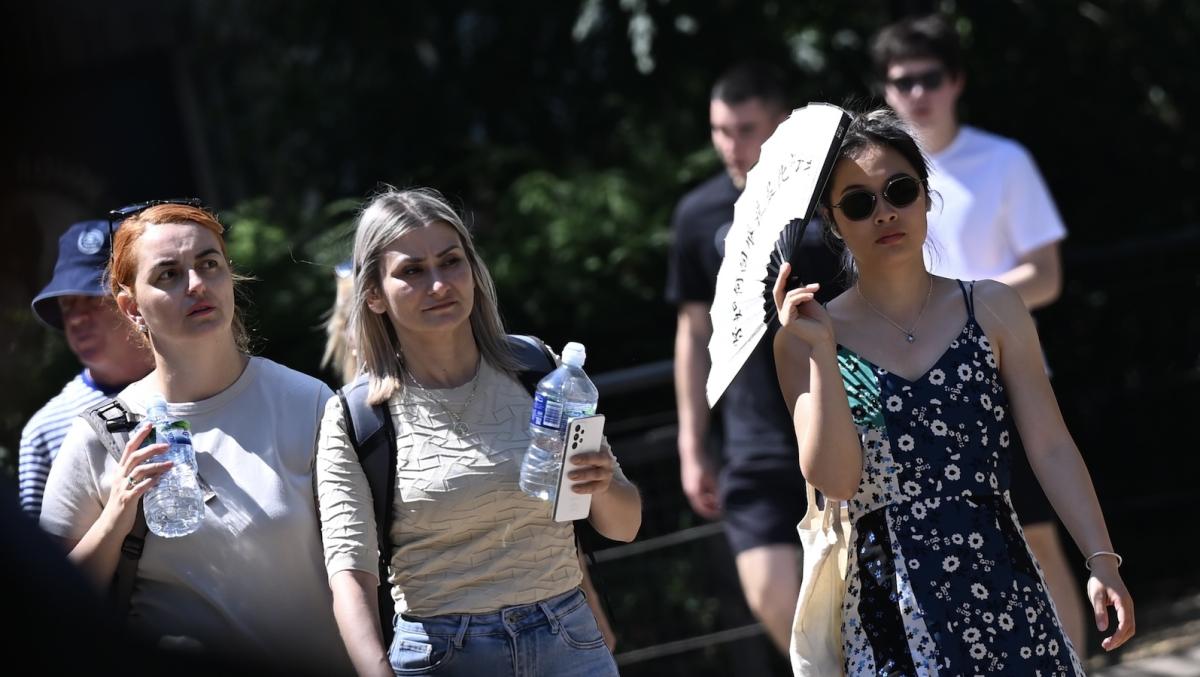 Pedestrians carry water bottles and fans under the sun