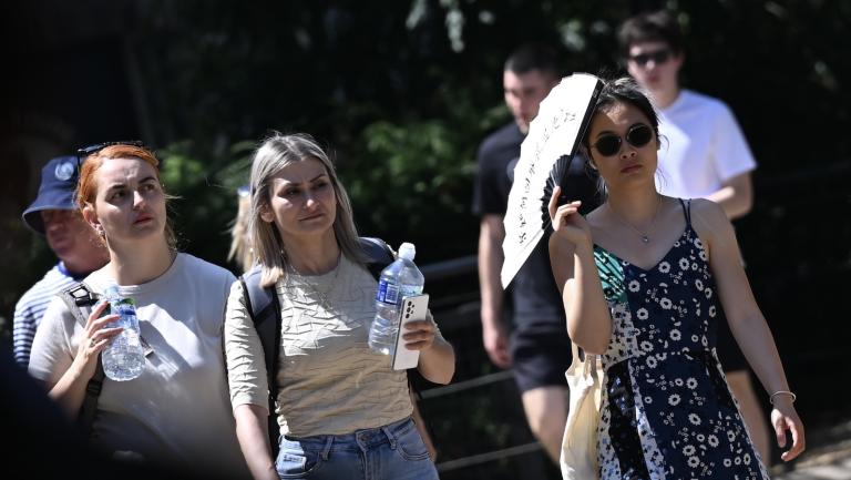 Pedestrians carry water bottles and fans under the sun