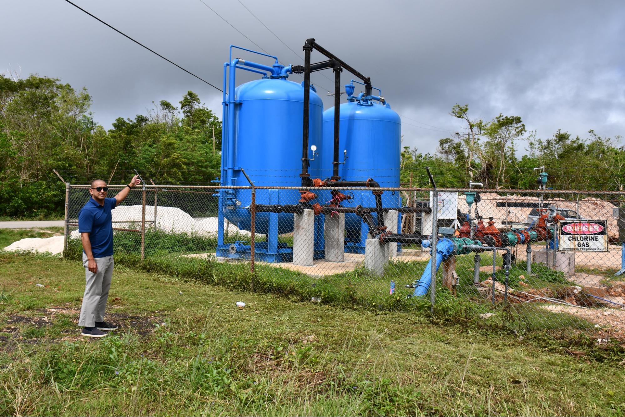 A man stands next to large blue water containers