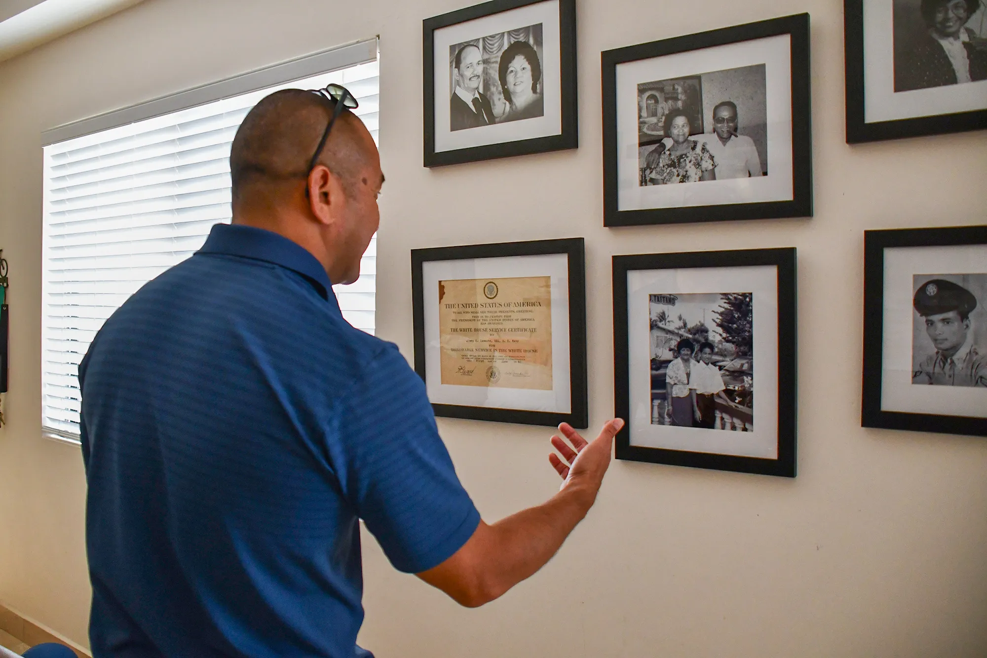A man stands in front of a gallery wall of photographs