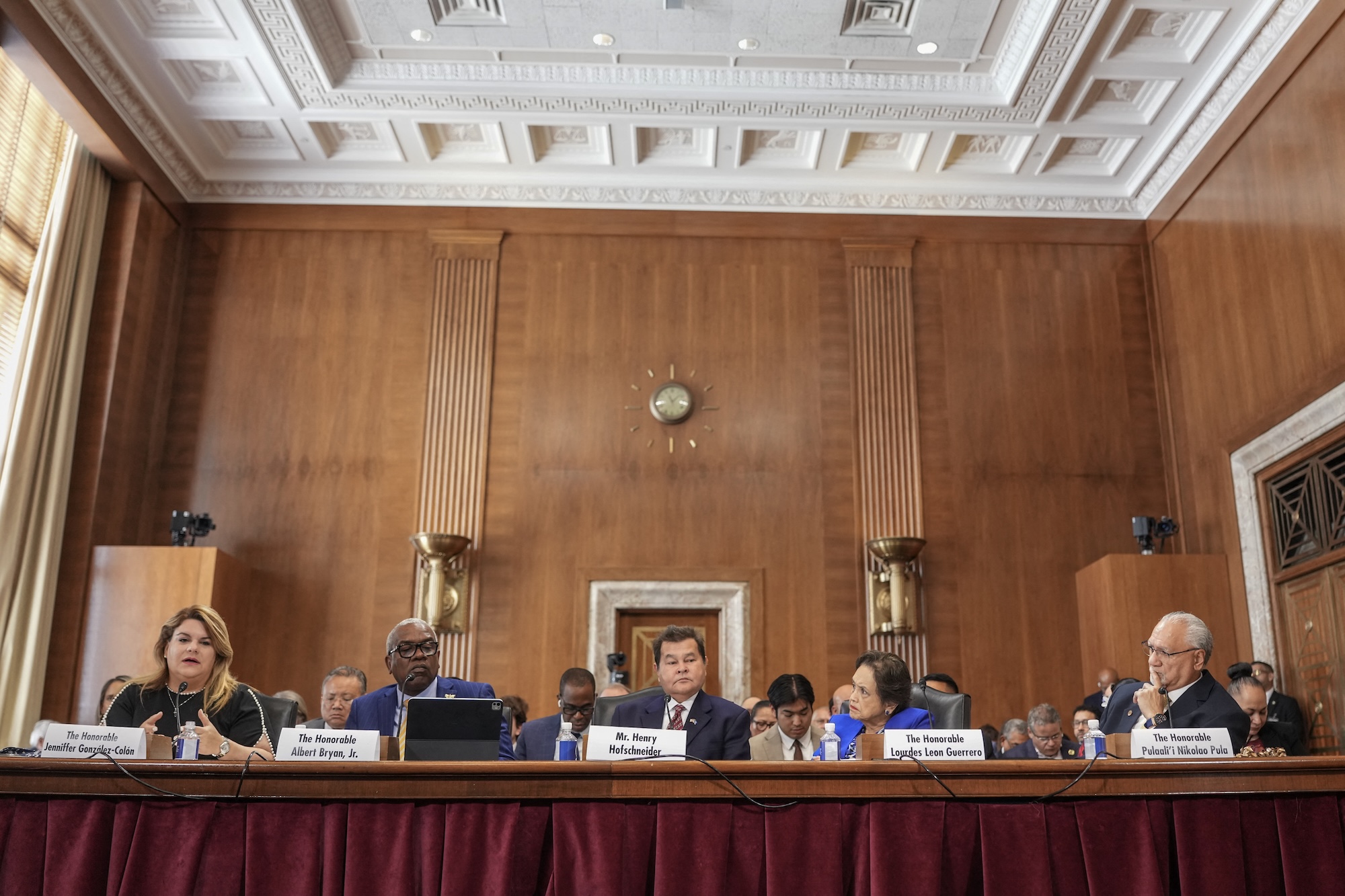 a group of people sit behind a long desk in a wood-paneled room