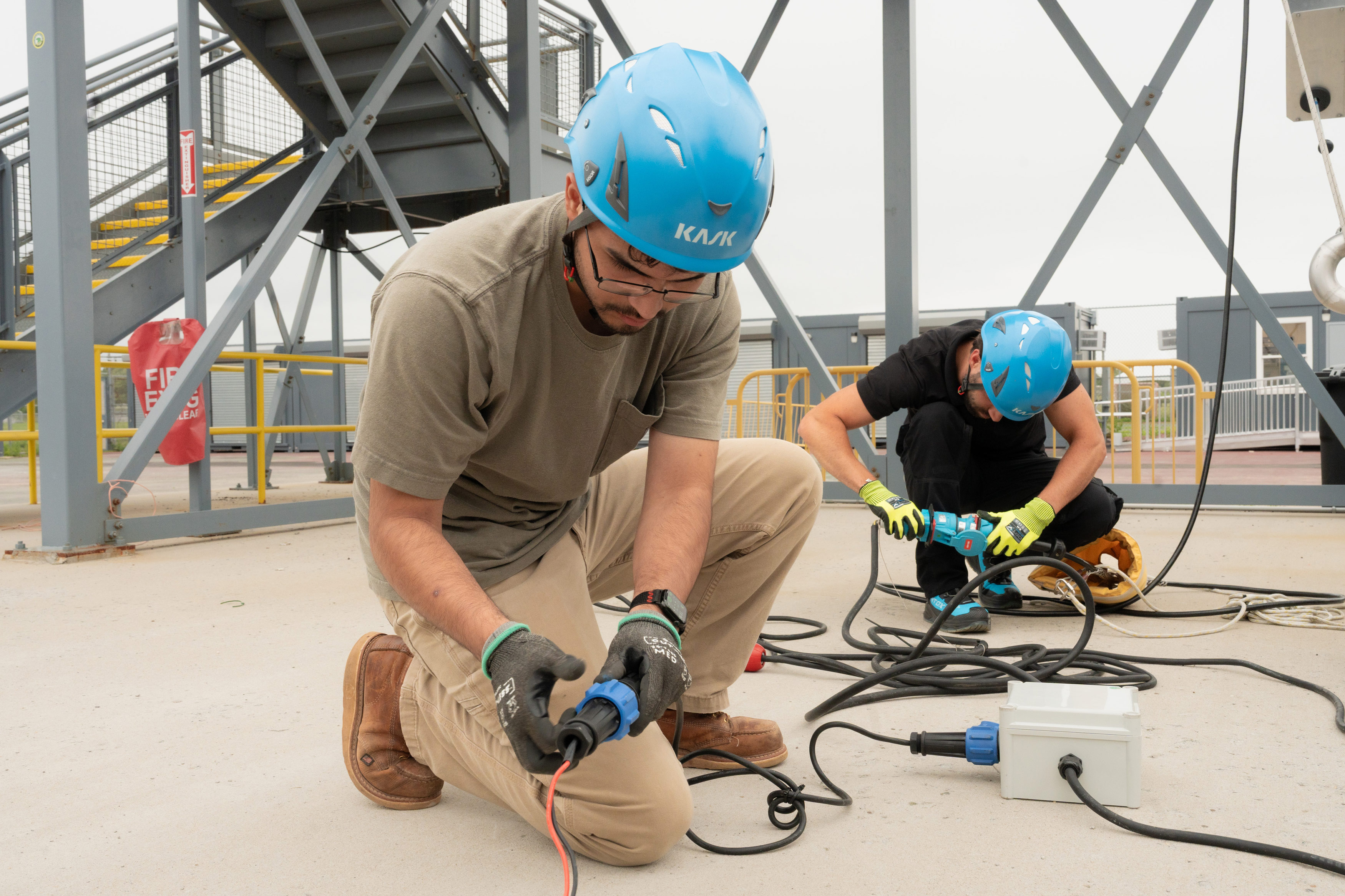 Two men in hard hats work work on an electrical line