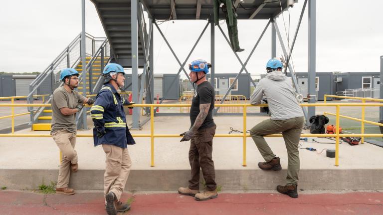 Four men in hard hats stand around talking