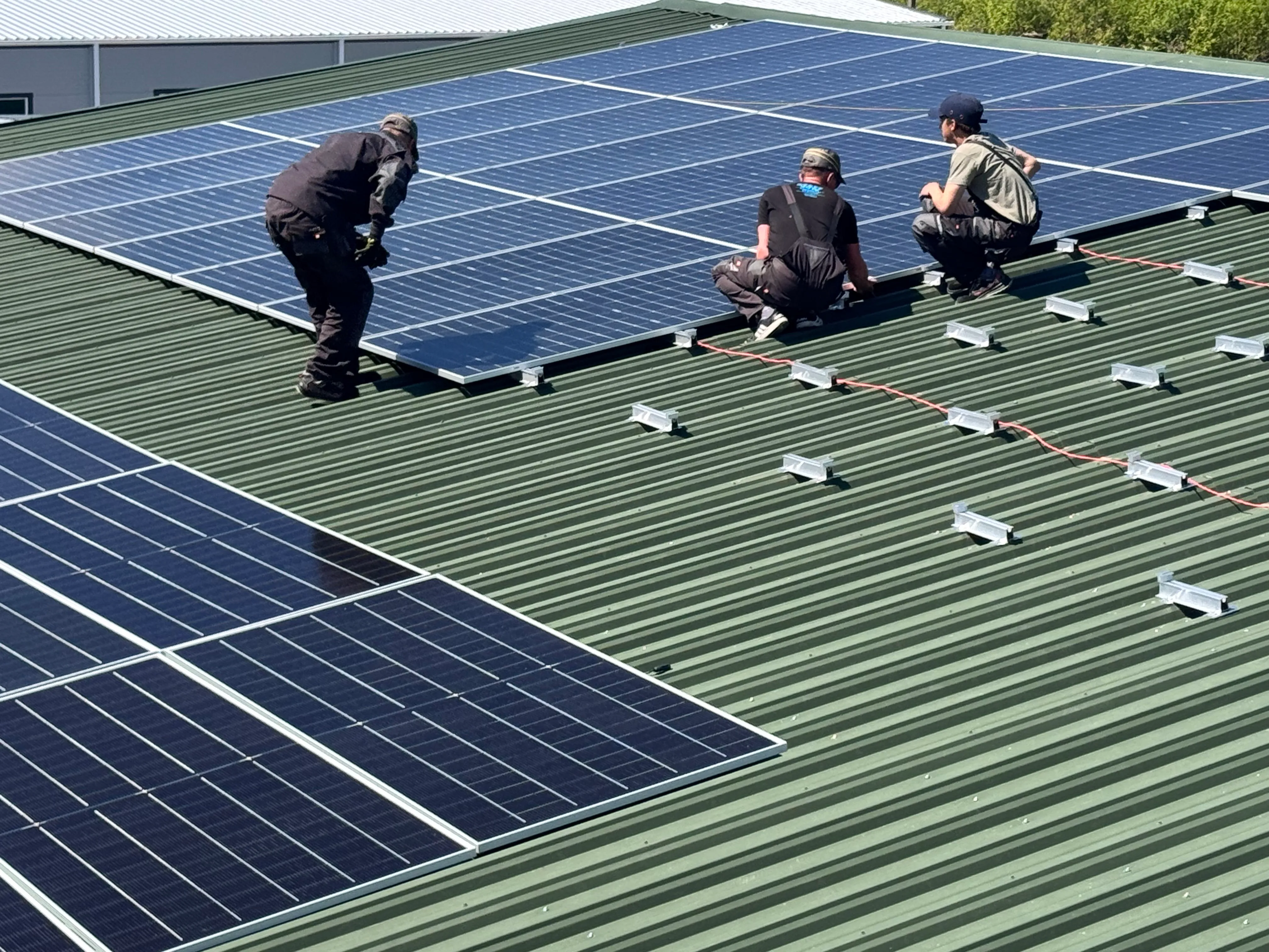 Three men on a rooftop installing solar panels