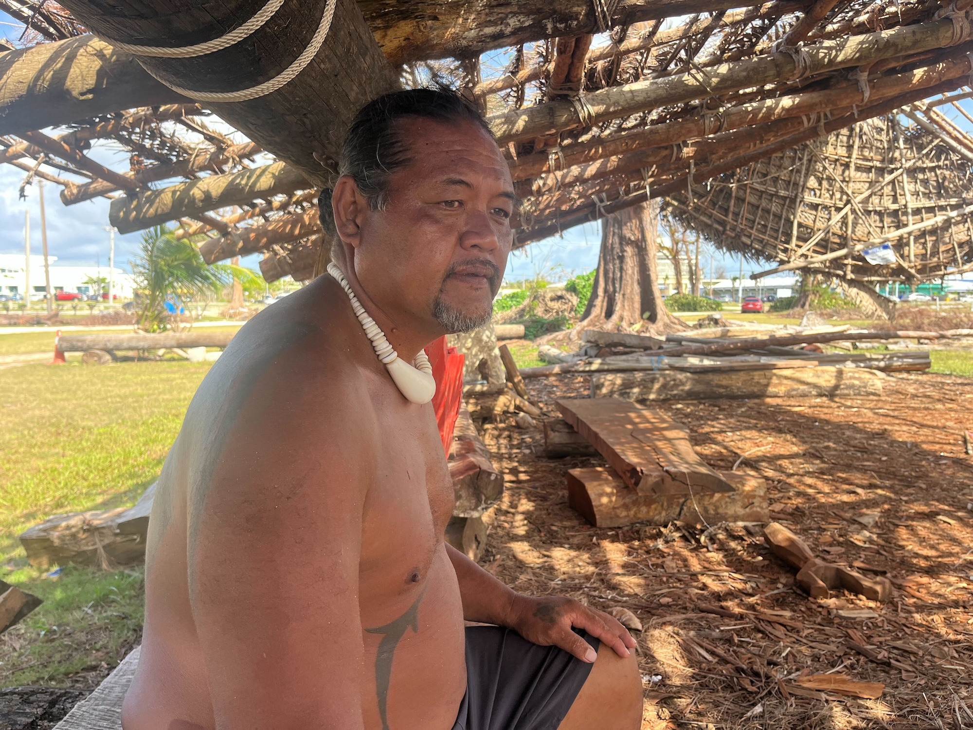 A man sits under a shelter made of natural materials