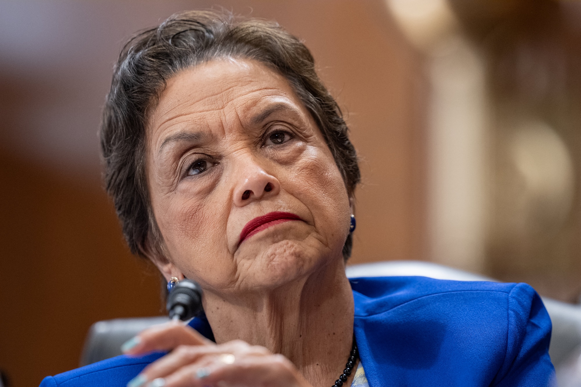 A woman in a blue suit listens during a committee hearing