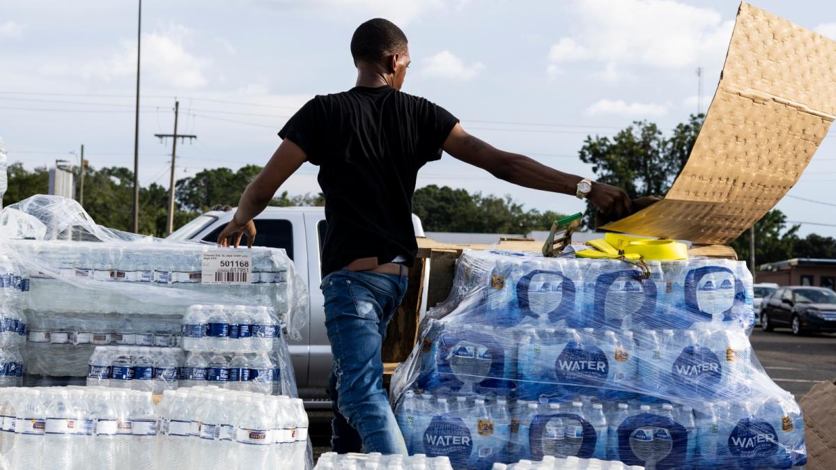 A man throws a cardboard box away amid piles of bottled water