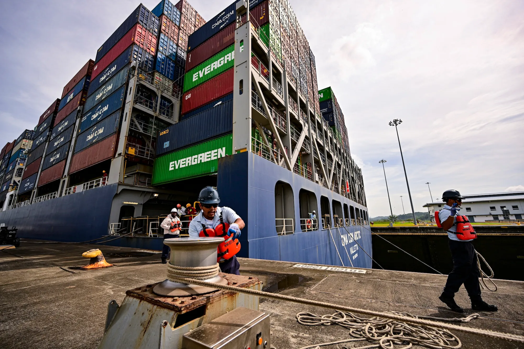 workers near a doc with shipping container vessel