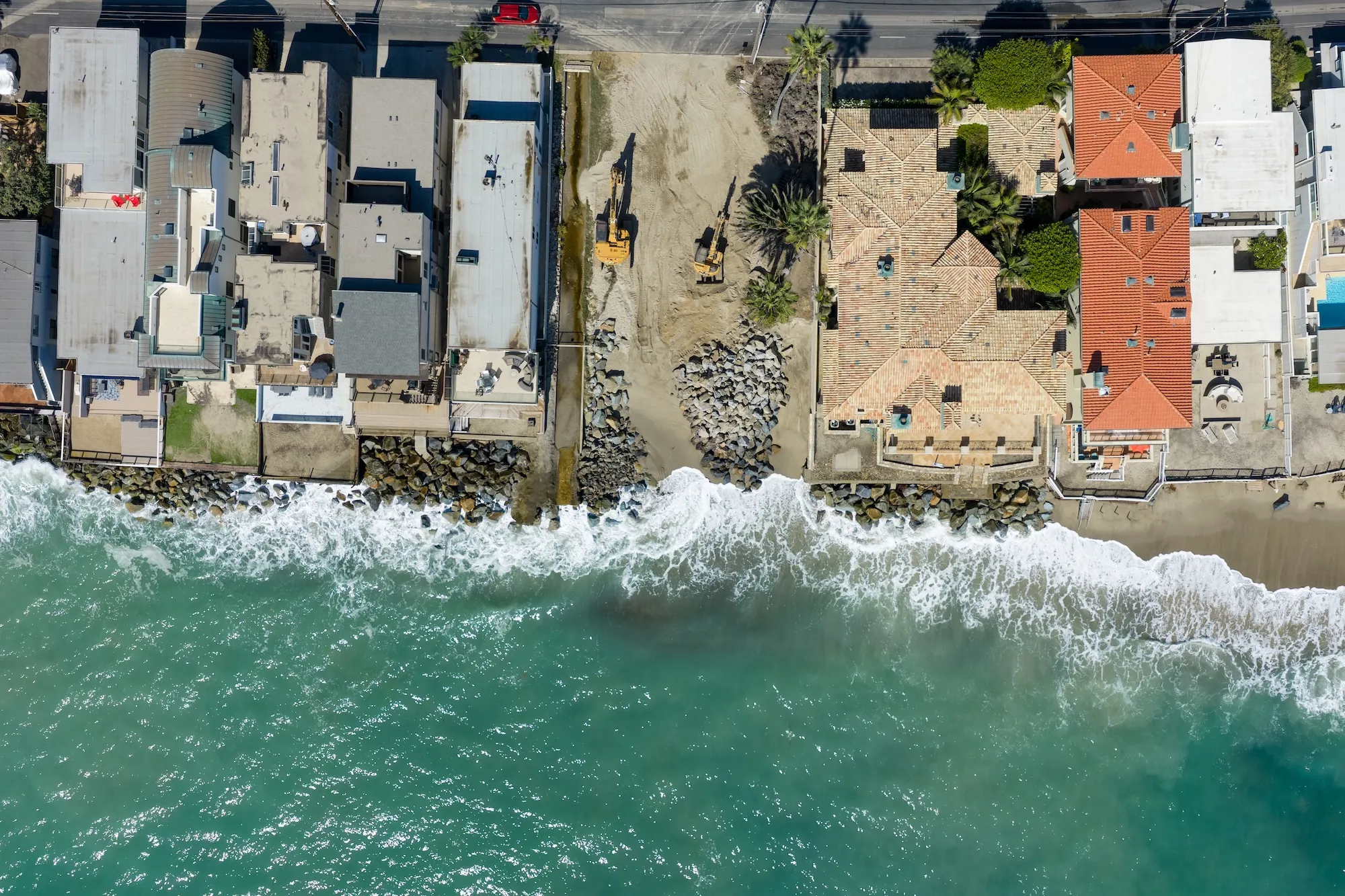 an aerial shot of waves crashing on a beach near houses with erosion