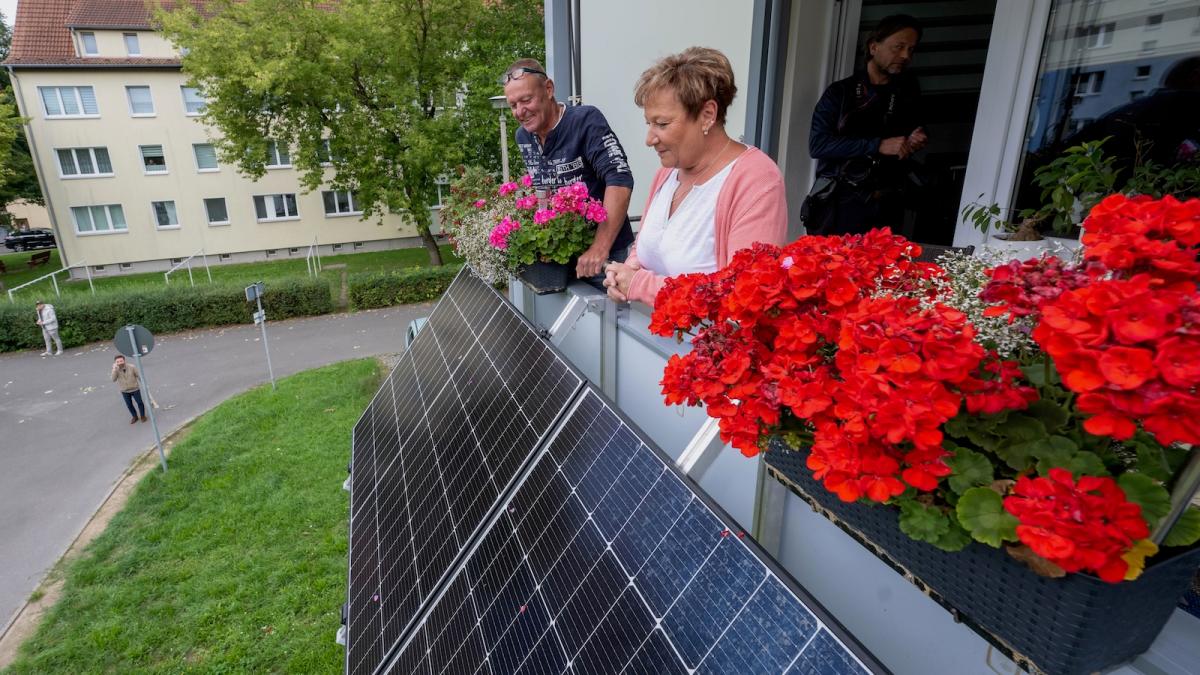 Two tenants of an apartment building inspect the solar panels mounted on their balcony.