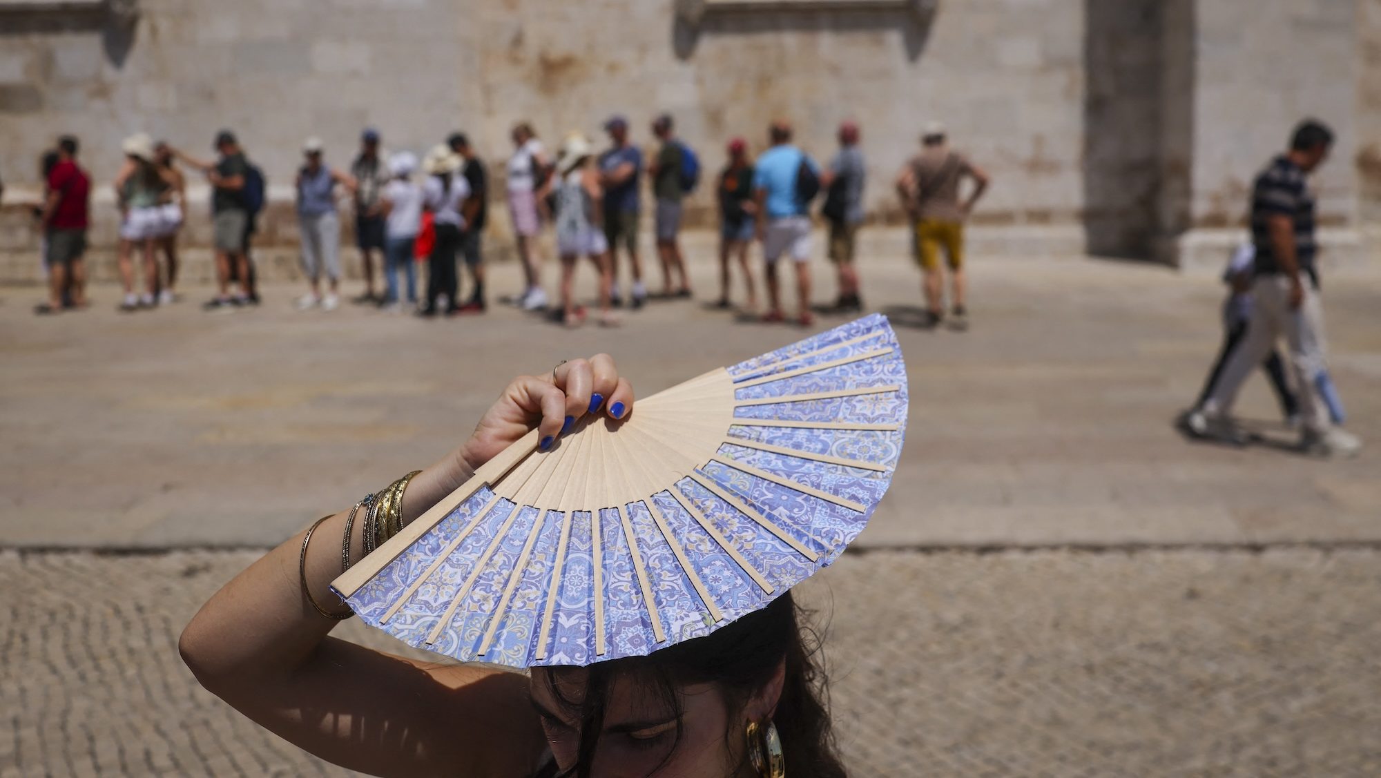 A woman holds up a fan to shield her head from the sun in front of a crowd
