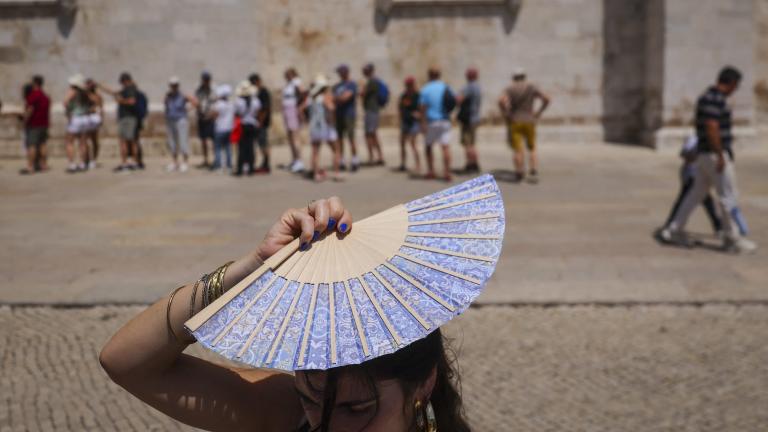 A woman holds up a fan to shield her head from the sun in front of a crowd