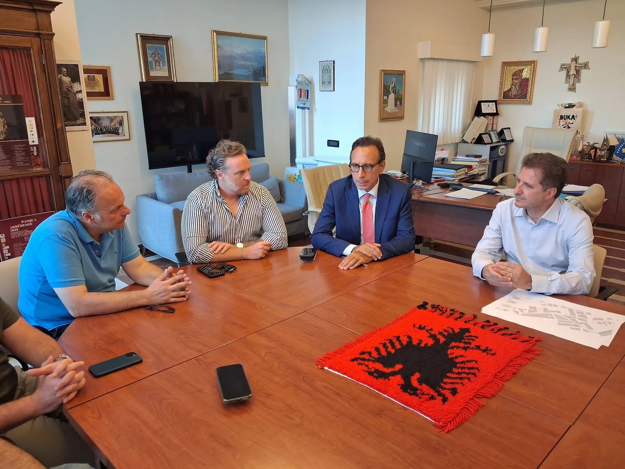 Men gather around a table with an Arbreshe symbol in the center