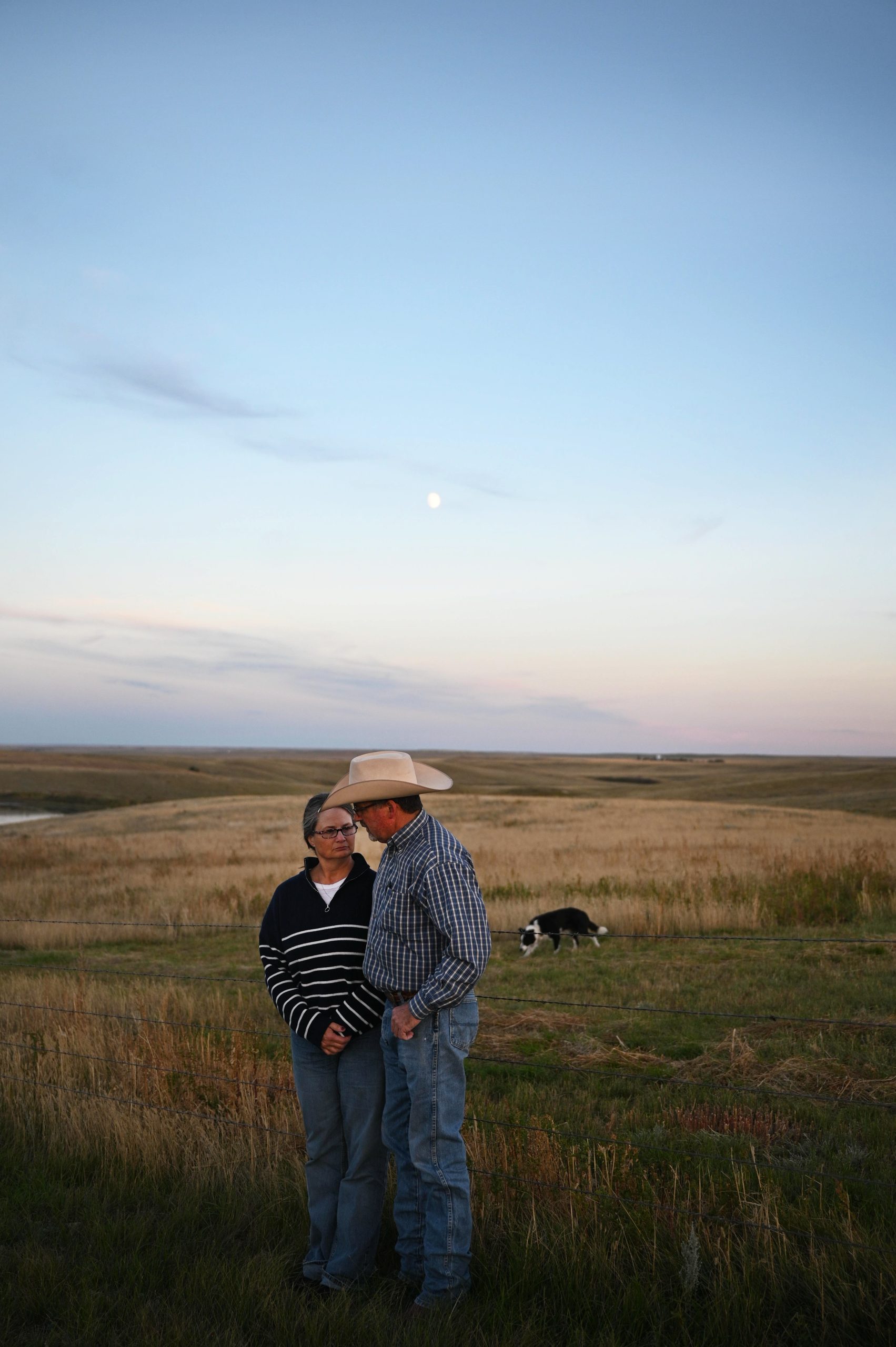 Tammi and Curtis Fladager standing beside a wire fence with a field behind them