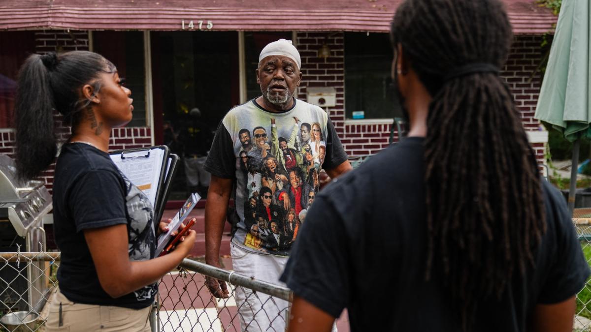 A young woman and a young man speak to an older man outside of his house