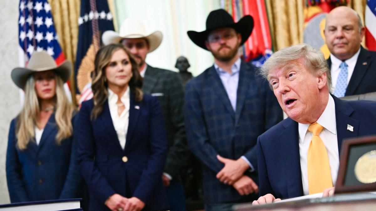 Donald Trump addresses the press from his desk in the Oval Office while men and women wearing suits and cowboy hats stand behind him