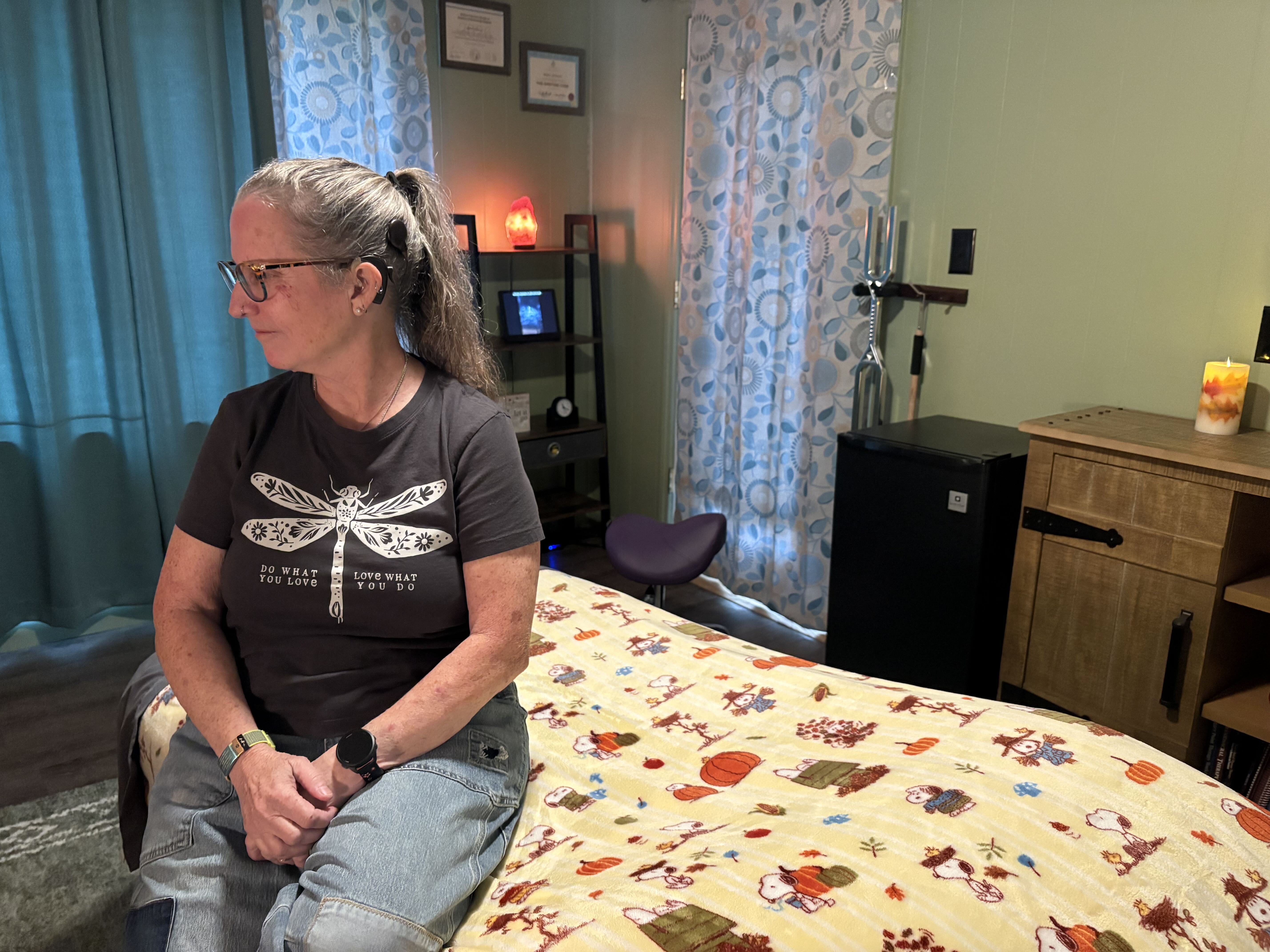 A woman with a cochlear implant sits on a bed