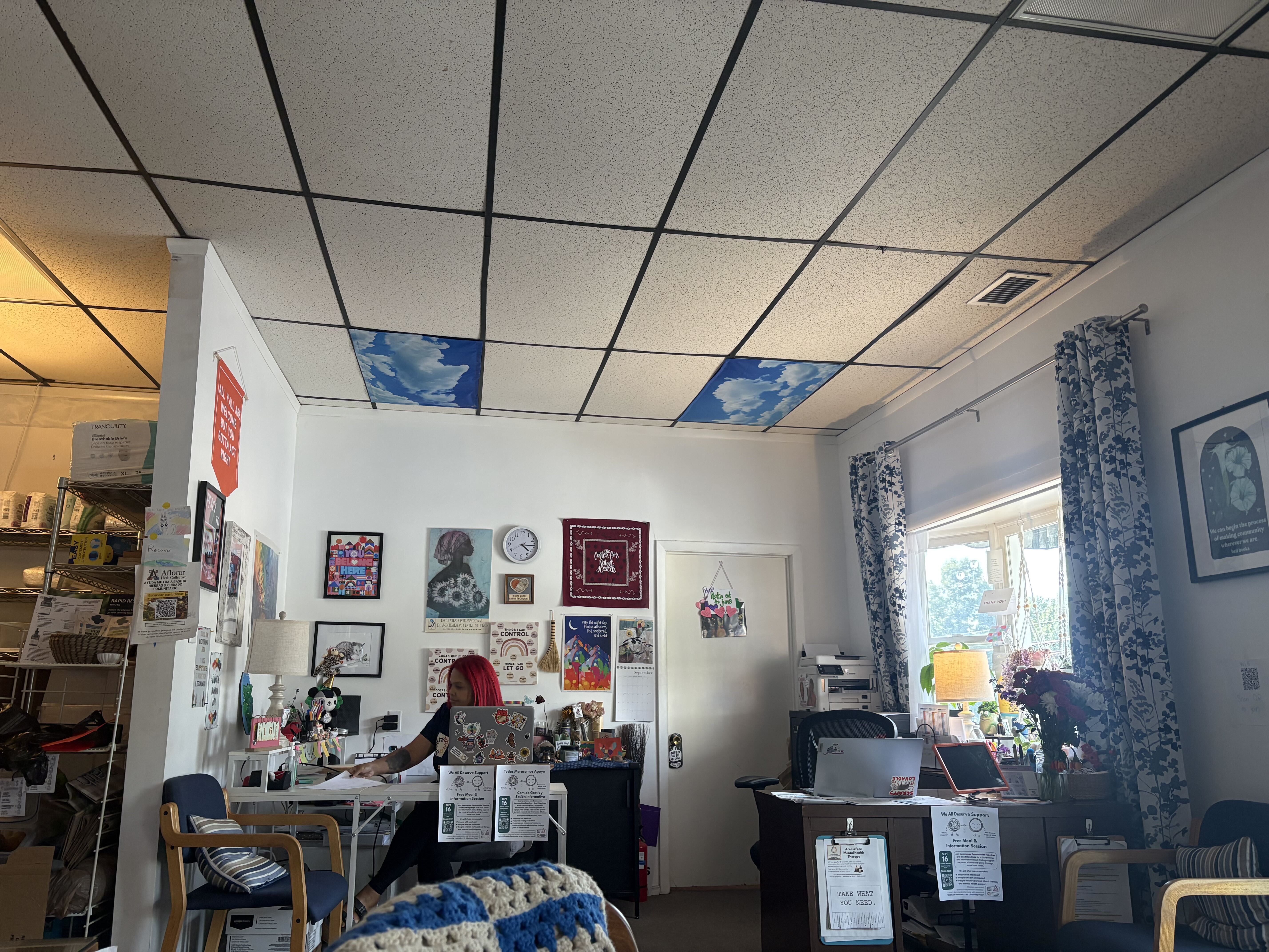 A woman sits in an office with lots of posters, cushions, and knick knacks