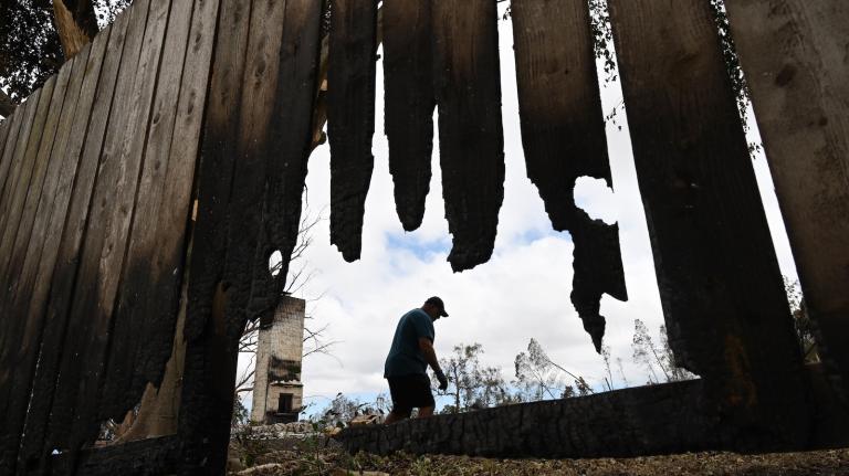 A man in Kula, Hawaii removes a fence burned in the wildfires that raced across Maui in 2023.