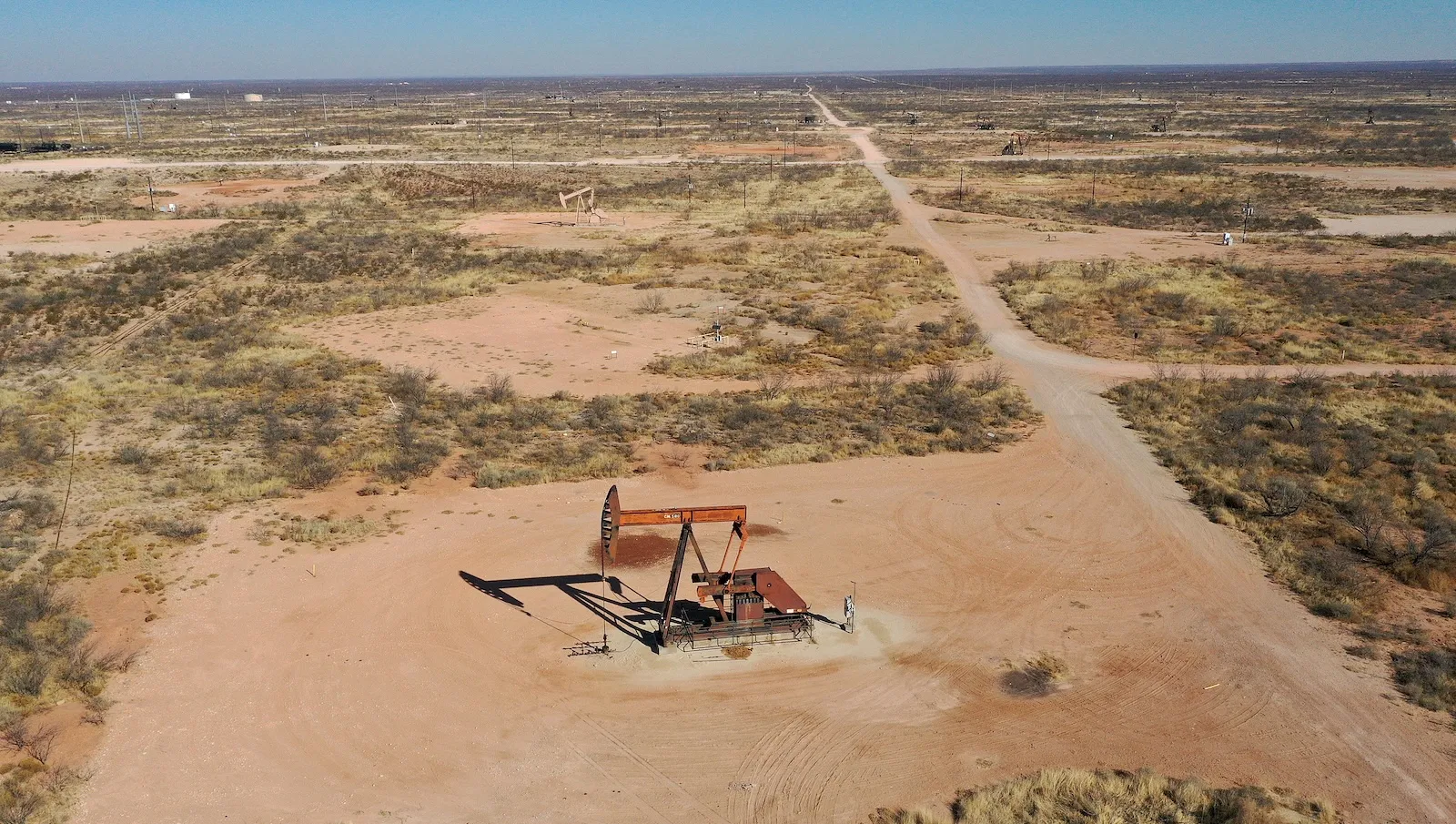a large piece of orange equiptment seen sitting on the sand from an aerial view with a scrubbing green landscape stretching out for miles towards the horizon line