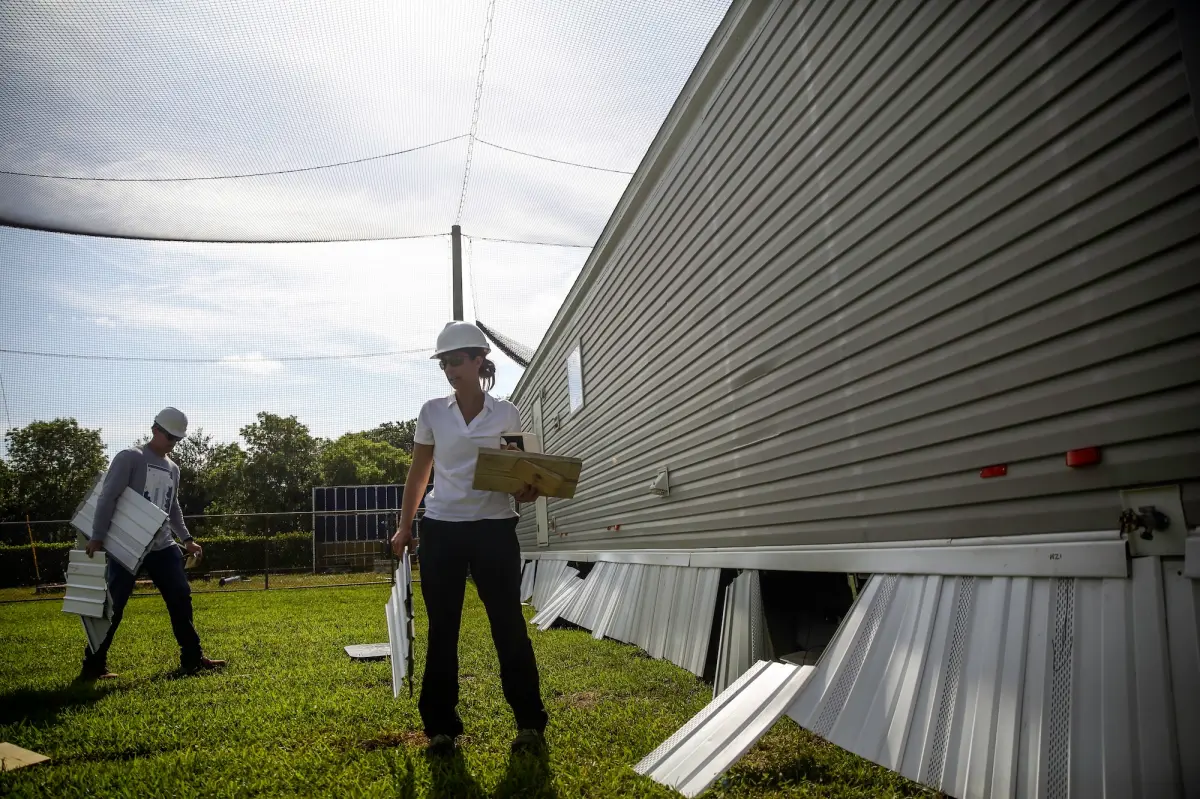 A woman stands near a manufactured home in a testing field for wind