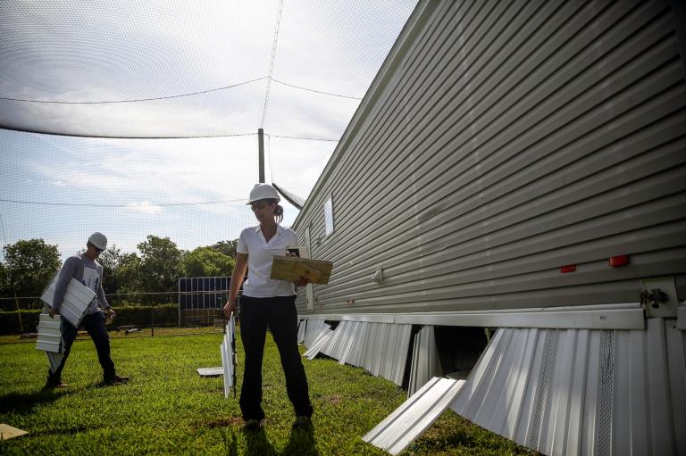 A woman stands near a manufactured home in a testing field for wind