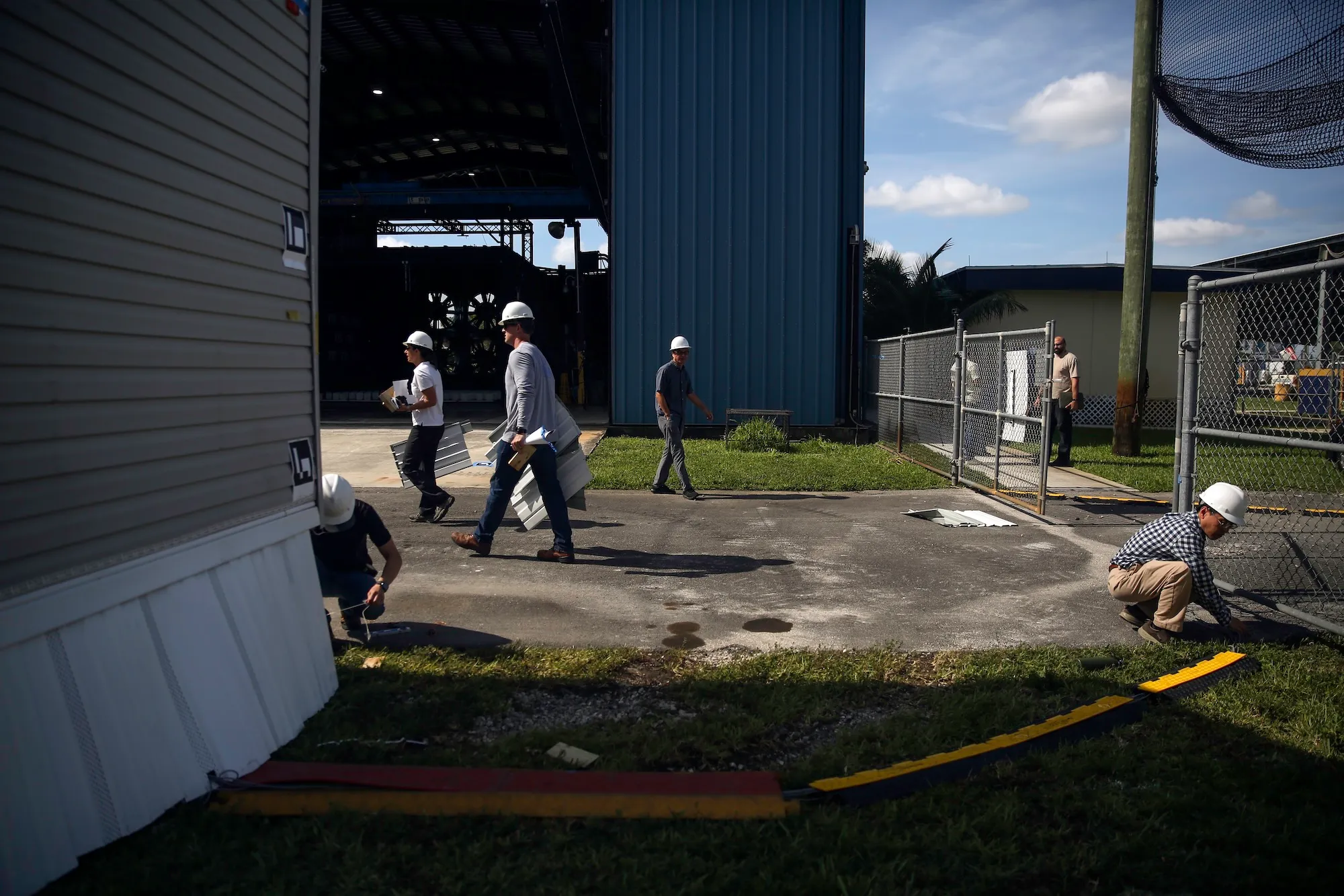 a group of people wearing hard hats walk around a corner near a wind testing site for manufactured housing