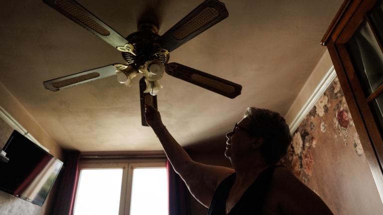 A woman turns on the ceiling fan in her bedroom.