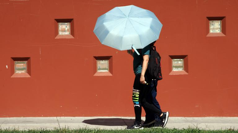 Two people holding an umbrella over them walking in front of a red building