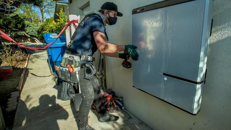 A technician installs a 215-pound lithium ion battery in a home in California.